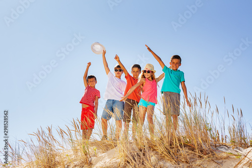 Group of happy kids wave from sand dune together