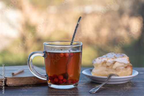 Tea glass with sweet cake and book on wooden table in the morning, outdoors