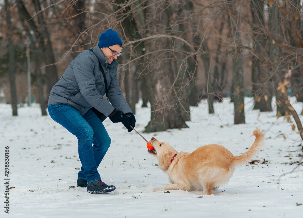Young man blowing snowflakes from her hands to her dog golden retriever in a winter day. Friendship, pet and human.