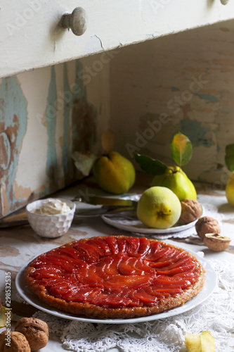 Quince tarte tatin served with whipped cream, quince fruits and walnuts on a wooden surface. Rustic style. photo