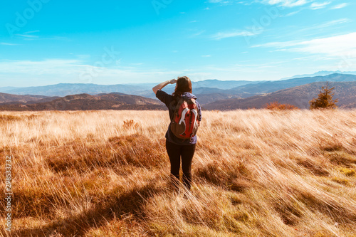 A girl in a jacket with a hood and a backpack looks into the distance at the panorama of autumn mountains, the concept of autumn travelling