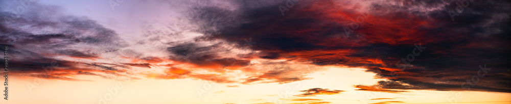Sunset sky background in yellow red and dark tones. Wide angle panorama of gloomy sky, banner format