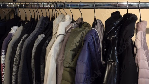 4K view of women's jackets hang on hangers in a row. A hand takes a hanger with a red jacket.