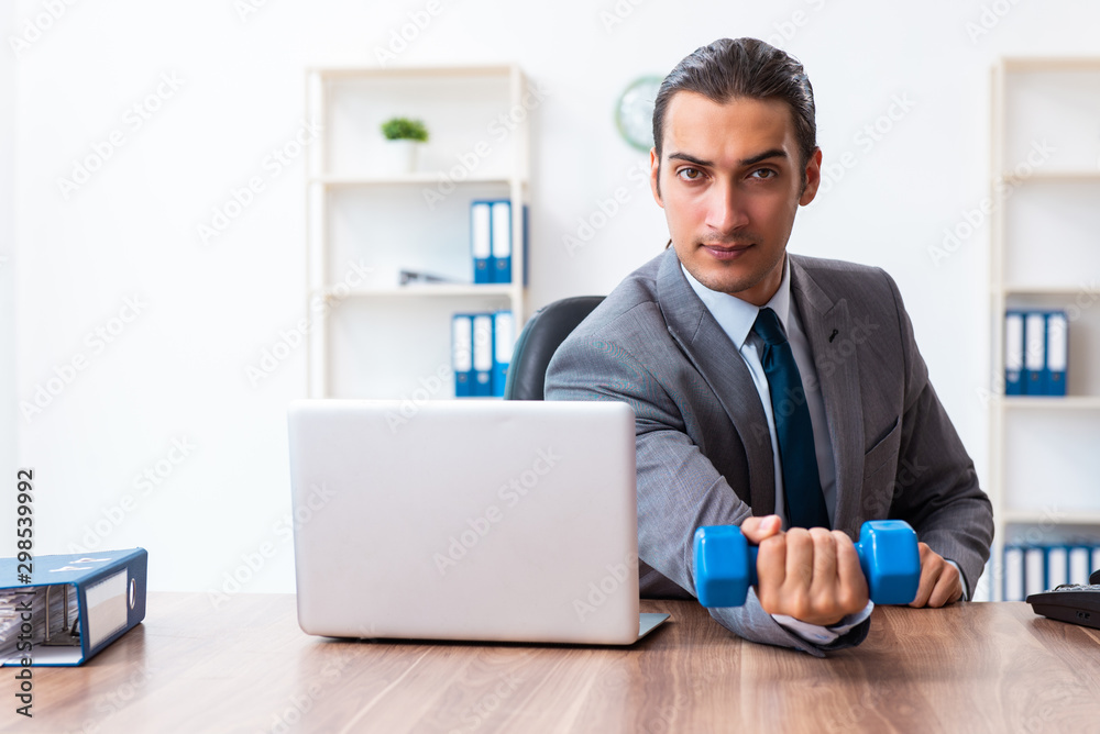Young handsome employee doing sport exercises at workplace Young handsome employee doing sport exercises at workplace