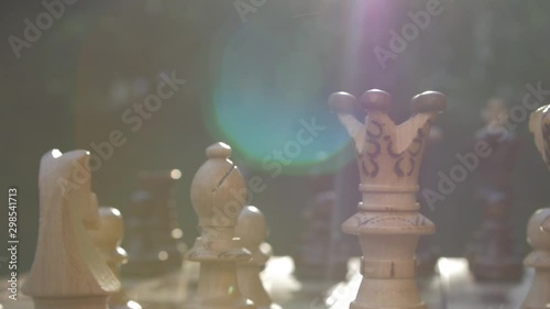Wooden chess game on a table in a camera slide from left to right against sun with lens flare