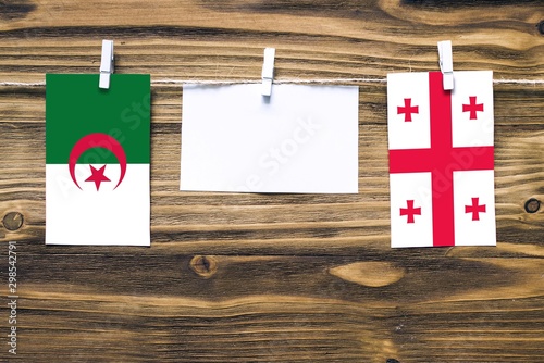 Hanging flags of Algeria and Georgia attached to rope with clothes pins with copy space on white note paper on wooden background.Diplomatic relations between countries.