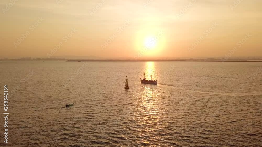 Fishing vessel on the background of golden sunrise. Long, narrow and fast racing sea kayak near fishing boat. Fishing vessel on the background of golden sunrise. Long, narrow and fast racing sea kayak near fishing boat.