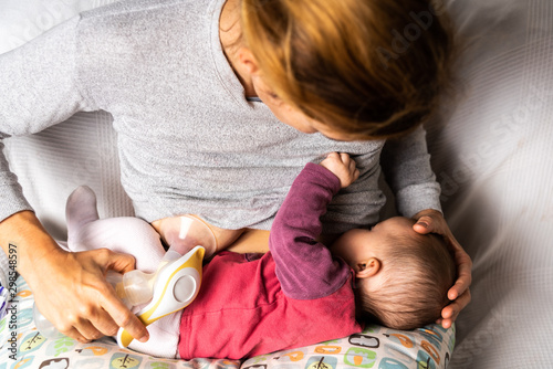 Mother breastfeeding her newborn baby while using a manual breast pump. photo