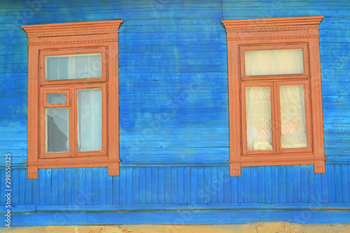 Old wooden windows on a log wall in bright blue. Decoration with carved clypeus. photo