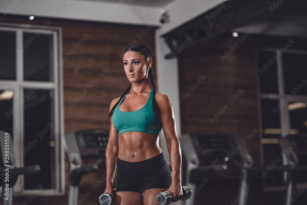 Fit girl in the gym with dumbbells.