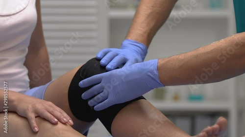 Therapist touching patient leg in compression knee brace, trauma rehabilitation