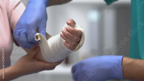 Physician putting elastic bandage on female patient arm, joint dislocation