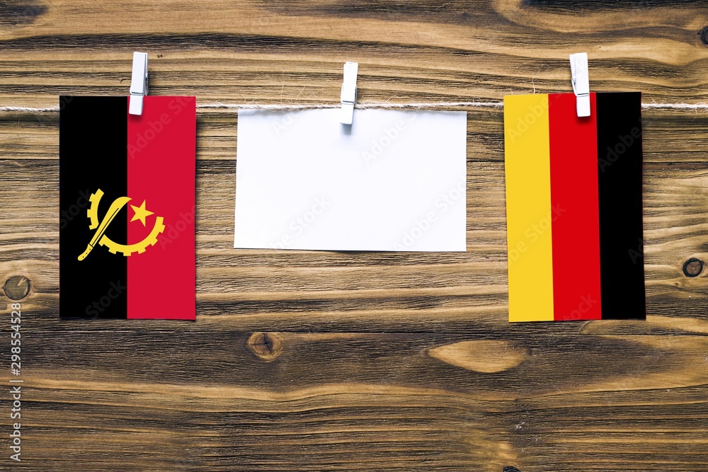Hanging flags of Angola and Germany attached to rope with clothes pins with copy space on white note paper on wooden background.Diplomatic relations between countries. Stock 写真 | Stock