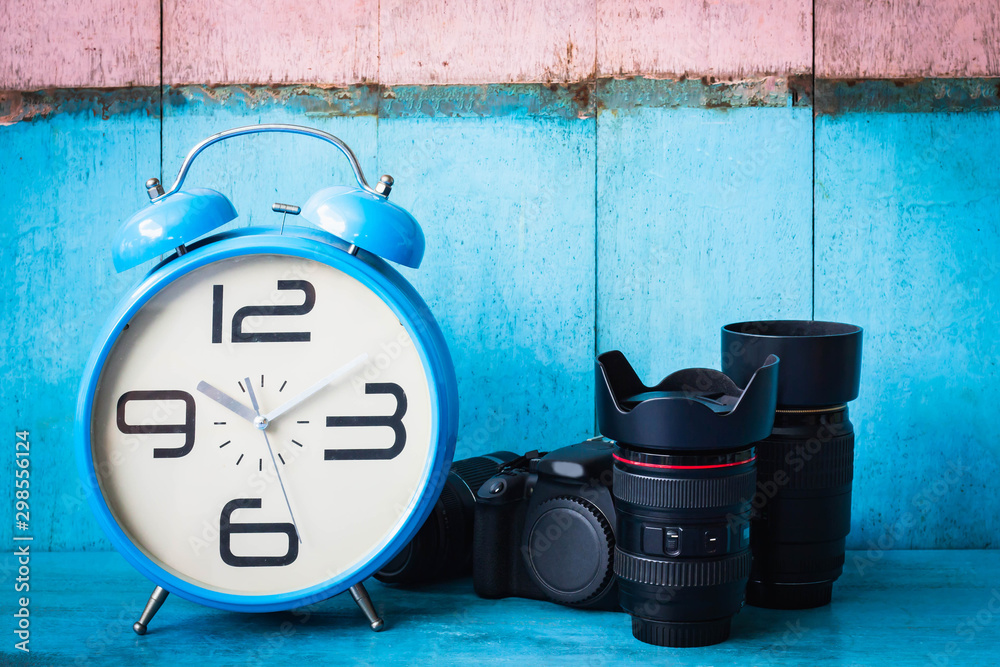 Blue vintage alarm clocks and digital camera on blue wooden table and light blue and pink background wall