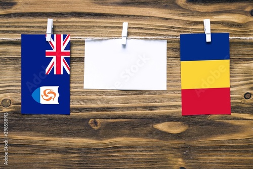 Hanging flags of Anguilla and Romania attached to rope with clothes pins with copy space on white note paper on wooden background.Diplomatic relations between countries.