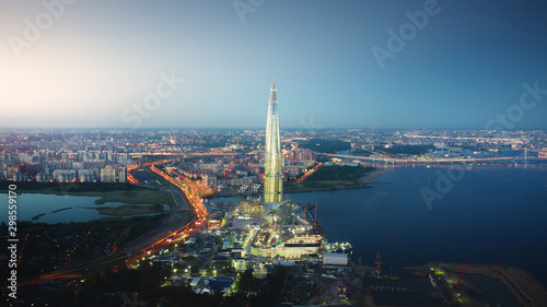 Beautiful motion of Lakhta Center in Saint Petersburg on the evening, view from above. Picturesque aerial panorama of the tower with bright glittering lights from buildings, streets and traf