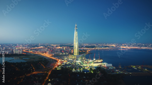 Beautiful motion of Lakhta Center in Saint Petersburg on the evening  view from above. Picturesque aerial panorama of the tower with bright glittering lights from buildings  streets and traf