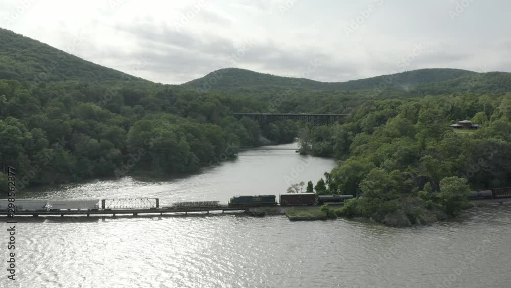 Drone shot of a long cargo train, flying to the left and following the train, with a bridge in the background. Drone shot of a long cargo train, flying to the left and following the train, with a bridge in the background.