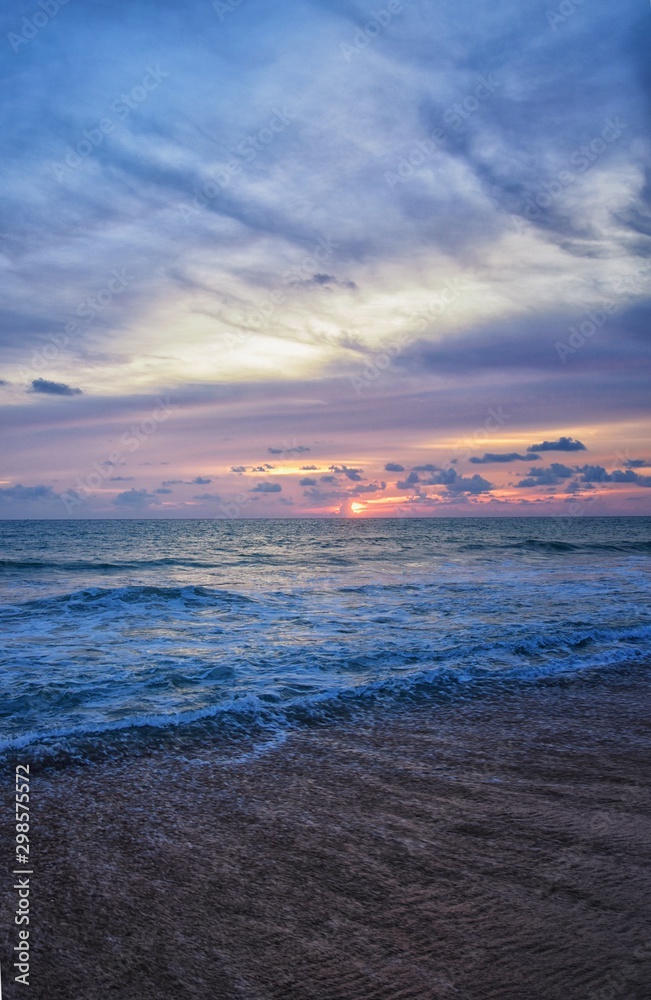 Phuket beach sunset, colorful cloudy twilight sky reflecting on the sand gazing at the Indian Ocean, Thailand, Asia.