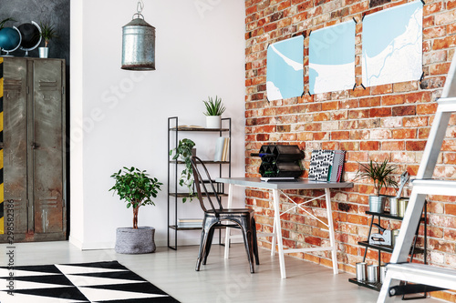 Maps on brick wall of industrial home office with metal furniture and wine rack on the desk