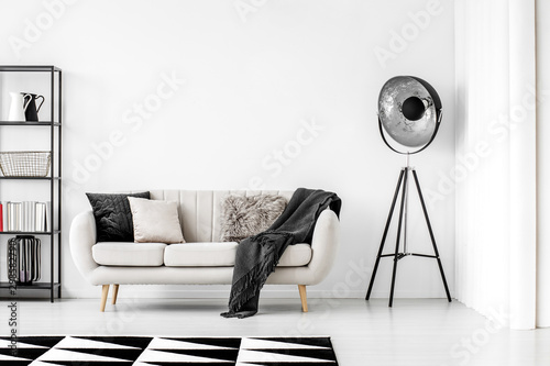 Poster Industrielle schwarze Lampe neben beige Couch mit Decke und Kissen,  Kopienraum auf leerer weißer Wand - Nikkel-Art.de