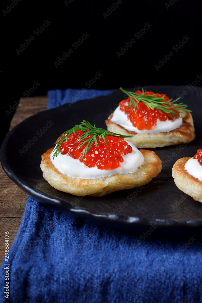 Pancakes with red caviar and cream cheese topped with dill on black plate Pancakes with red caviar and cream cheese topped with dill on black plate