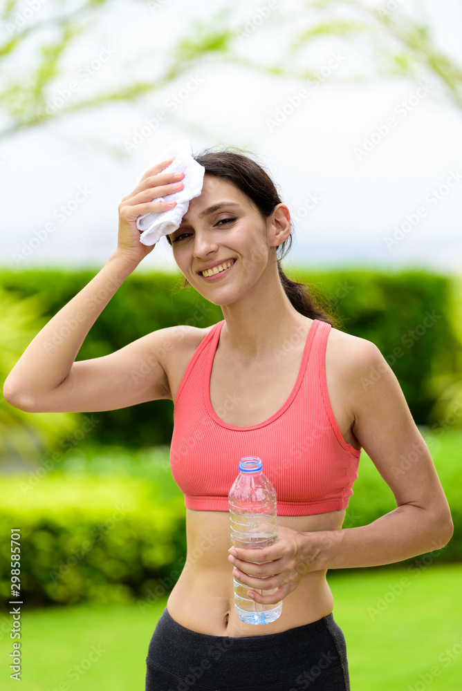 Beautiful woman runner has tired and rest for drinking water and a white towel to wipe her face after running in the garden. Beautiful woman runner has tired and rest for drinking water and a white towel to wipe her face after running in the garden.