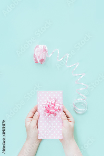 Hands holding a pink gift box on pastel mint desk