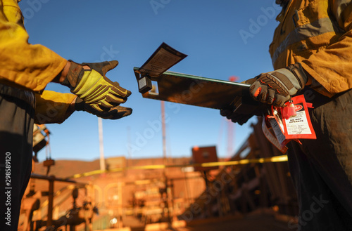 Senior miner supervisor dress as work uniform hand over safety isolation lock box permit to work board to workmate during shift changing on two weeks shut down operation mine site Perth, Australia 