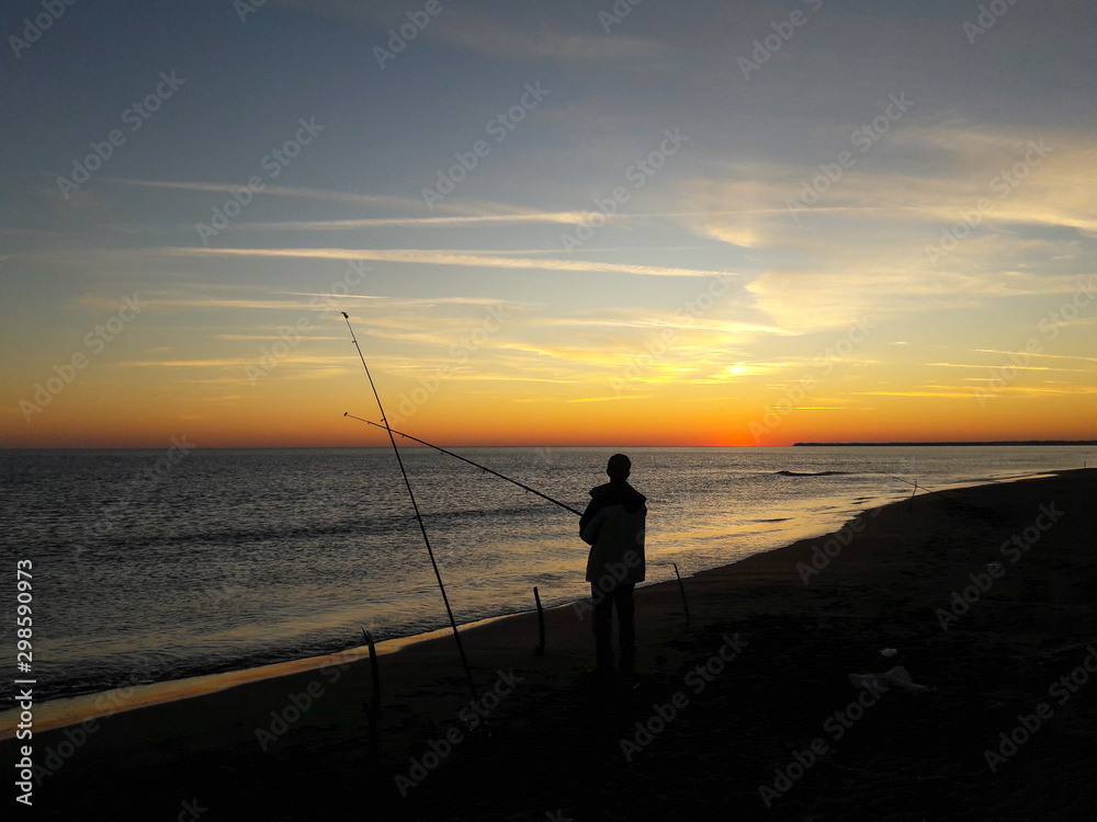 Fishing man silhouette on the seashore during sunset
