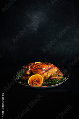 Baked whole chicken with oranges and rosemary. Tray with a festive Christmas dish on a black table and black background. Low key. Vertical. Copyspace
