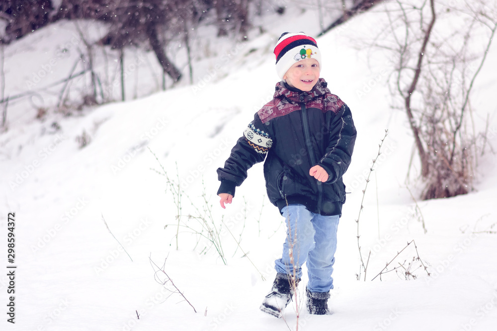 Little smiling boy in a winter hat runs through the snow in snowy weather