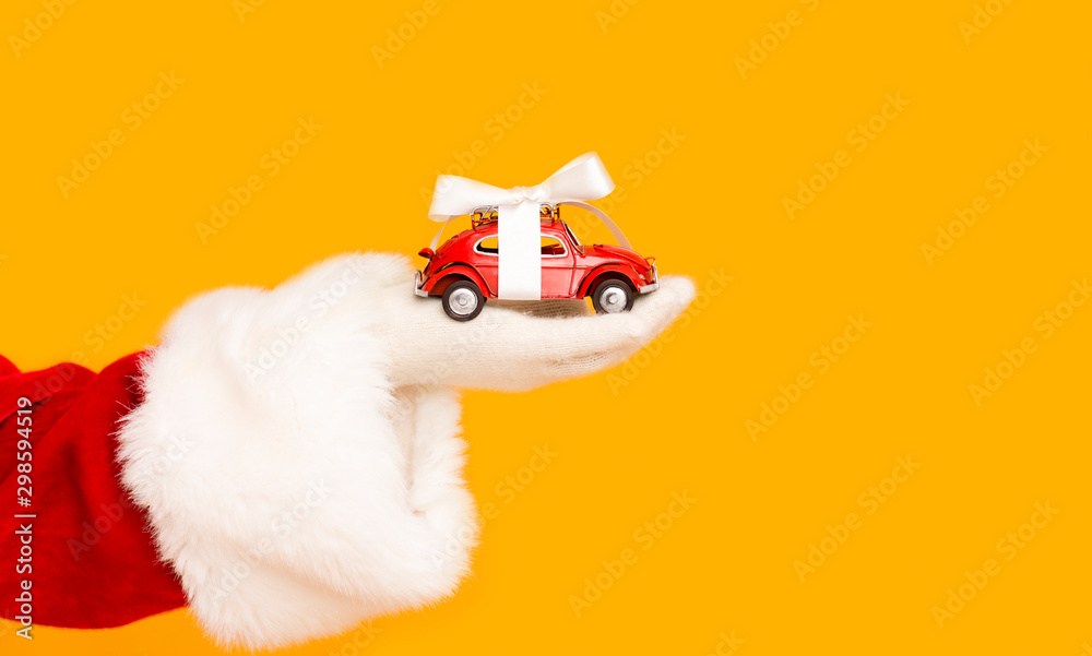 Santa Claus holding modern car with bow in hand over orange - obrazy, fototapety, plakaty 