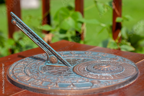Antique sundial with a beautiful dial and ornament. The bronze oxidized disk is located on a wooden base. Selective shallow focus on the center of the disc.