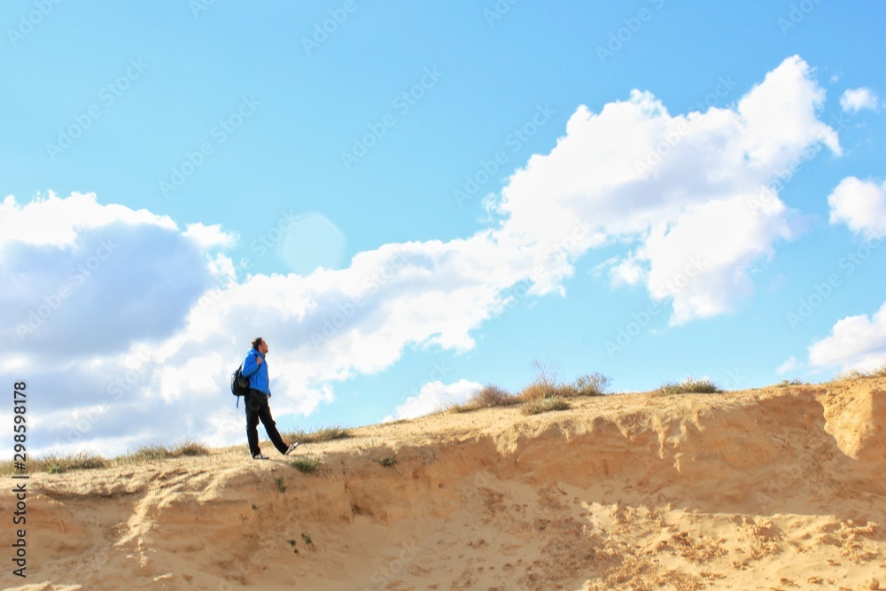 Solo traveling man with backpack on the sand dune with sky background 