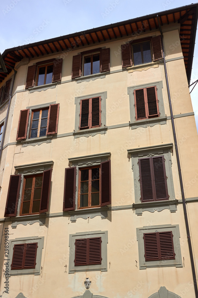 Facade of house with yellow wall, windows with brown shutters in Firenze, Italy.