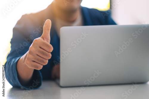 Businessman showing thump up while working on laptop in office