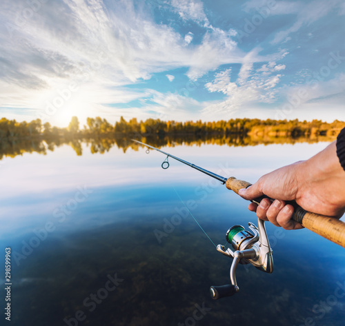 hand with spinning and reel on the summer lake