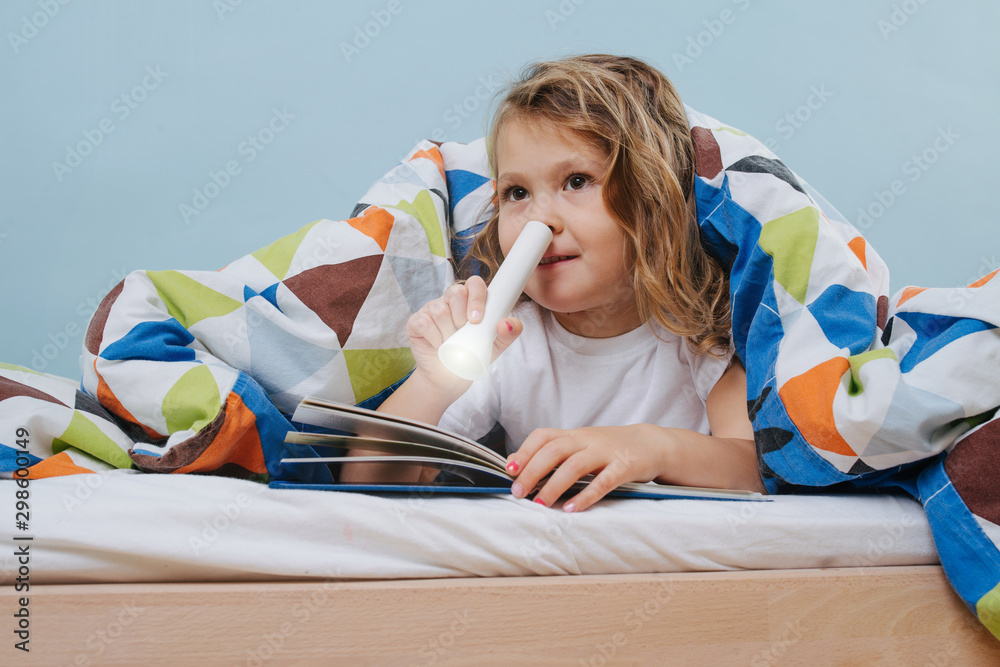 Adorable little girl reading in bed with flashlight under blanket Adorable little girl reading in bed with flashlight under blanket