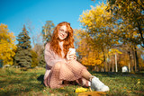 Portraits of a charming red-haired girl with glasses and a pretty face. Girl posing in autumn park in a sweater and a skirt of coral color.