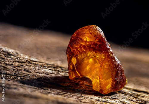 Natural amber. A piece of yellow transparent natural amber on large piece of dark stoned wood. photo