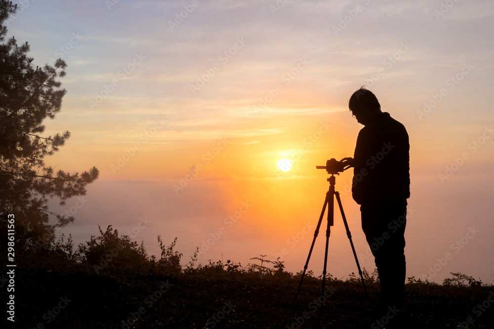 Silhouette of photographer take photos with mirror camera on peak of mountain. misty landscape, spring orange pink misty sunrise in beautiful valley below.