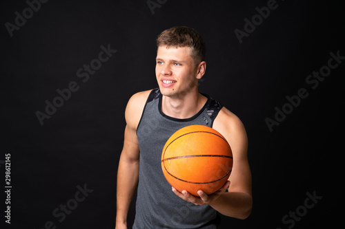 Handsome young man playing basketball over isolated black wall