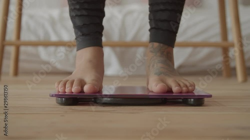 Close-up of barefoot black female legs checking body weight on weighing scale in domestic room. Positive slimming african american woman on scales controlling progress of weighloss dieting program. photo