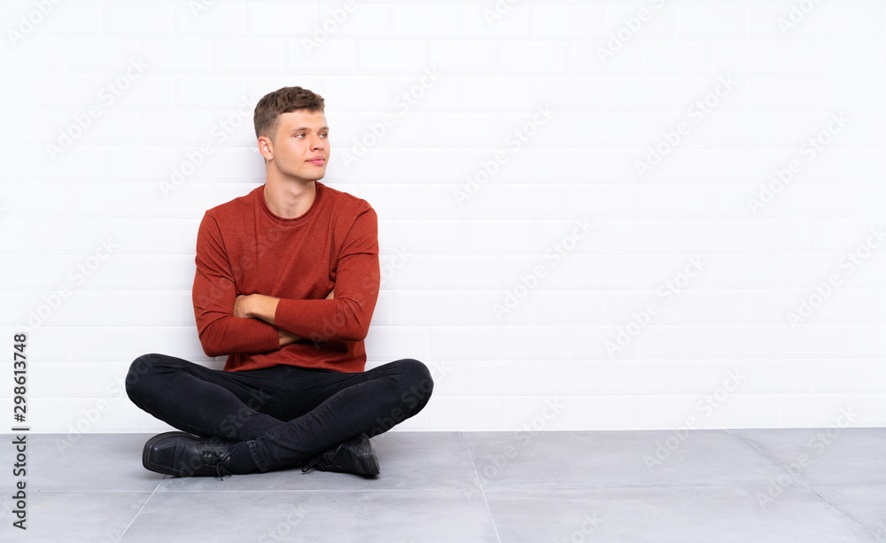 Young handsome man sitting on the floor looking to the side Young handsome man sitting on the floor looking to the side