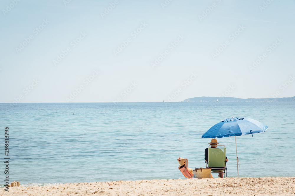 un homme assis sur la plage à Porquerolles sous un parasol regarde la mer