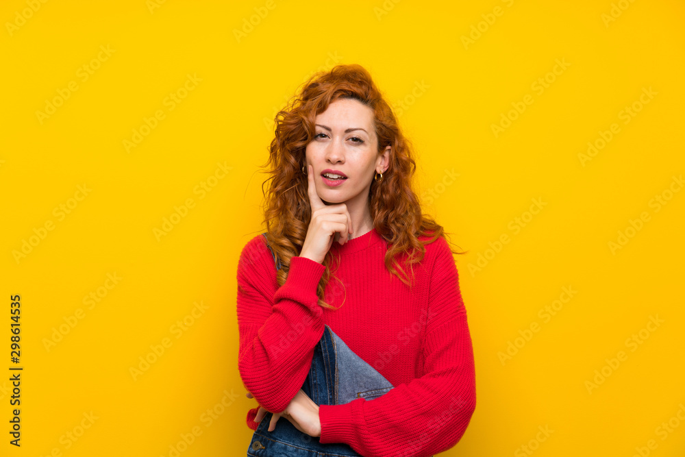 Redhead woman with overalls over isolated yellow wall thinking an idea Redhead woman with overalls over isolated yellow wall thinking an idea