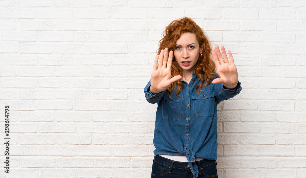 Redhead woman over white brick wall making stop gesture and disappointed Redhead woman over white brick wall making stop gesture and disappointed