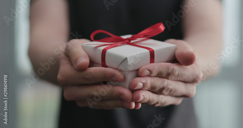 young man shows white paper gift box with red ribbon