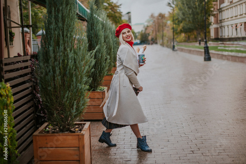 Pretty young woman in white coat and red beret joy and happy. Dancing near outdoor  city cafe